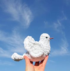 a white crocheted bird sitting on top of someone's hand under a blue sky