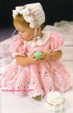 a baby doll wearing a pink crochet dress and bonnet holding a green ball