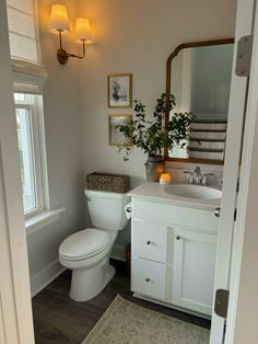 a white toilet sitting next to a sink in a bathroom under a mirror and lights