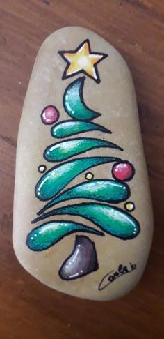 a hand painted rock with a christmas tree on it and stars above the top, sitting on a wooden surface