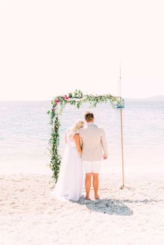 a bride and groom standing under an arch on the beach