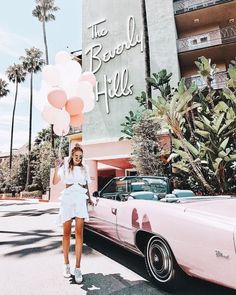 a woman standing next to a pink car with balloons in the shape of a heart