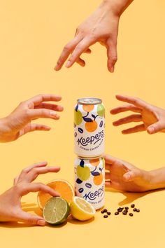 several people reaching out their hands to grab an orange and lime soda from a can