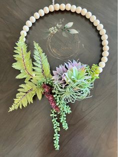 a necklace with plants and beads hanging from it's side on a wooden table