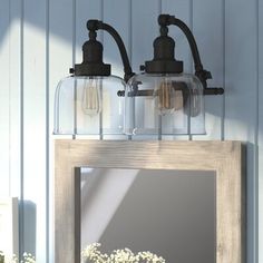 two lights are attached to the wall above a mirror and vase with flowers in it