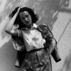 a woman leaning against a wall with her hand on her head and looking at the camera