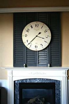 a clock on the wall above a fireplace in a room with white walls and black shutters