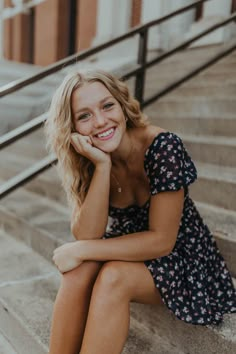 a woman sitting on the steps in front of stairs smiling at the camera with her hand under her chin