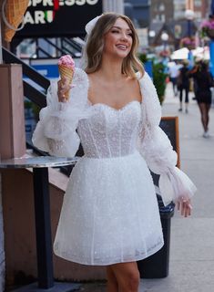 a woman in a white dress is holding an ice cream cone and posing for the camera