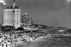 many people are on the beach and in the water near buildings with tall spires