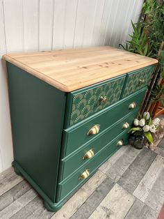 a green dresser with gold knobs on the drawers and wood top, next to a potted plant