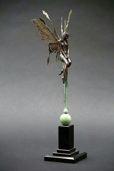 a sculpture of a fairy with wings on top of a green ball and black base