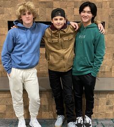 three boys standing next to each other in front of a brick wall with their arms around one another