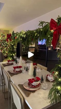 a dining room table set for christmas with red and white plates, silverware and greenery