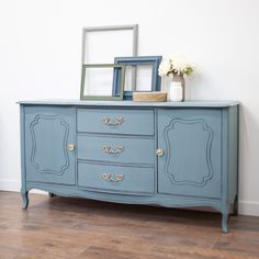 a blue dresser with two frames on top and flowers in vases sitting on top