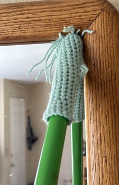 a crocheted green toothbrush holder in front of a mirror with a wooden frame