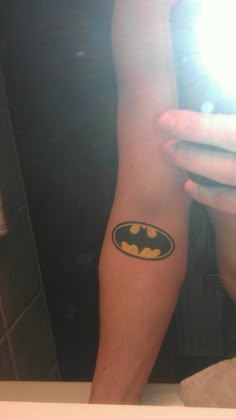 a person with a batman tattoo on their arm taking a selfie in the mirror