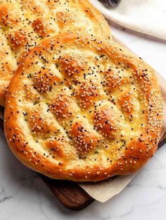 two sesame seed breads on a wooden cutting board with olives in the background