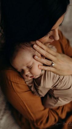 a woman holding a baby in her arms while laying on the bed with it's eyes closed