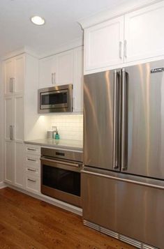 a kitchen with white cabinets and stainless steel refrigerator freezer combo in the center, along with hardwood flooring