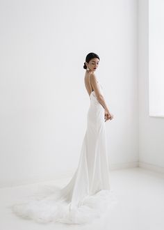 a woman in a white dress is standing near a window and looking off to the side