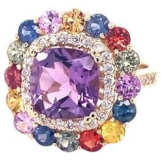 7.13 Carat Cushion Cut Amethyst Sapphire Diamond Yellow Gold Cocktail Ring Amethyst, Multi-Colored Sapphires and Diamond Cocktail Ring! A beautiful and sparkly combination of colorful beauty! This one of a kind piece has been carefully designed and curated by our in house designer! This ring has a vibrant Cushion Cut Amethyst that weighs 3.55 Carats and is embellished with 16 Multi-Colored Sapphires that weigh a total of 3.02 Carats as well as 38 Round Cut Diamonds that weigh 0.56 Carats (Clarity: SI1, Color: F). The total carat weight of the ring is 7.13 Carats. The ring is crafted in 14 Karat Yellow Gold and weighs approximately 9.1 Grams. The ring is a size 7 and can be re-sized at no additional charge. Luxury Amethyst Ring With Cushion Cut Center Stone, Luxury Cushion Cut Purple Jewelry, Colored Sapphires, Yellow Gold Cocktail Ring, Diamond Cocktail Ring, Gold Cocktail Ring, Gold Cocktail, Diamond Cocktail Rings, Fantasy Jewelry