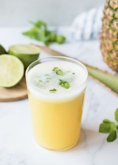 a pineapple drink in a glass next to sliced limes and a wooden spoon