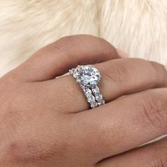 a woman's hand with a diamond ring on top of her finger, and a white fur background