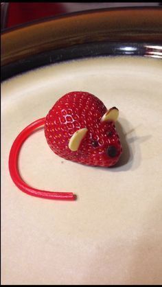 a toy mouse made out of strawberries sitting on top of a white plate with red handles