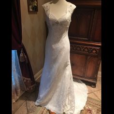 a white wedding dress on display in front of a wooden cabinet and rug with flowers