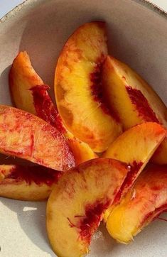 sliced peaches in a white bowl on a table with red stuff all over them