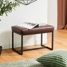 a brown leather bench sitting on top of a wooden floor next to a potted plant