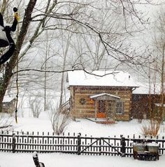 a snowboarder doing a trick in front of a log cabin on a snowy day