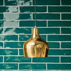 a gold colored light hanging from a chain in front of a blue brick wall with green tiles