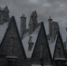 an old building with snow on the roof and chimneys in front of it, under a cloudy sky