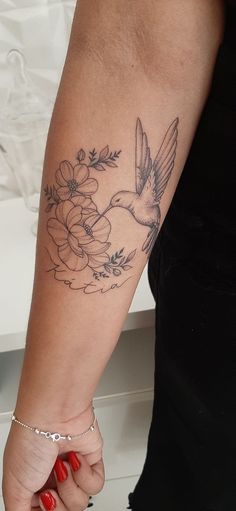 a woman's arm with a bird and flowers tattoo on the left side of her arm