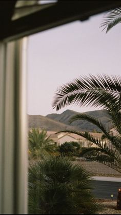 a view out the window of a house with mountains in the background and palm trees