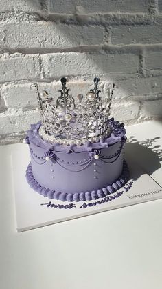 a purple cake with a tiara on top is sitting next to a brick wall