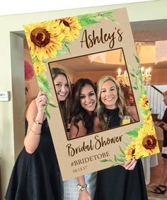 two women holding up a photo frame with sunflowers on it