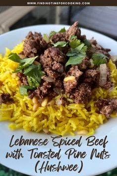 a white plate topped with yellow rice and meat next to a green leafy garnish