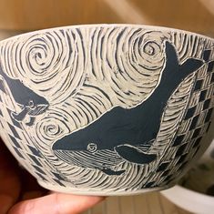 a hand holding a bowl with a whale design on it