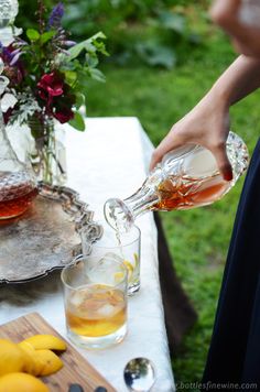 a person pours tea into a glass on a table with lemons and flowers