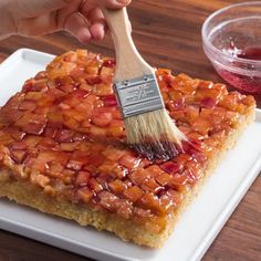 a person is holding a brush over a piece of cake on a plate with strawberry toppings