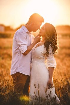 a man and woman standing next to each other in a field with the sun setting behind them