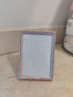 a pink and white photo frame sitting on top of a counter next to a vase