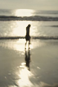 the silhouette of a person standing in the water at the beach with the sun behind them