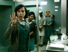 a woman standing in front of a mirror making the v sign with her hands while other people look on