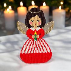 a beaded christmas angel ornament on a table with candles in the background