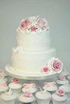 a wedding cake and cupcakes with pink roses on the top are sitting on a table