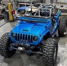 a blue jeep with four wheels in a factory room next to other cars and machinery